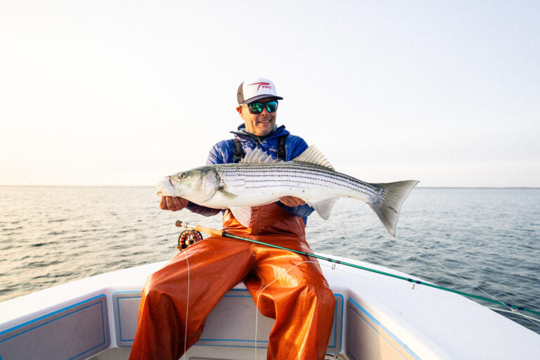 Man on a boat holding a large fish with a clear sky and water background