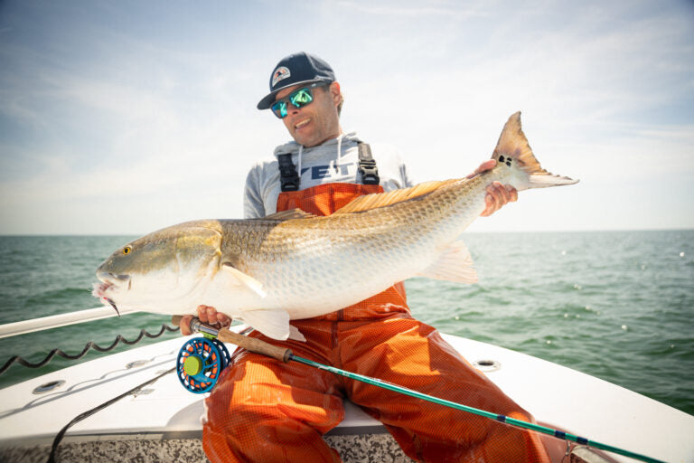 Man holding a large fish on a boat with ocean in the background