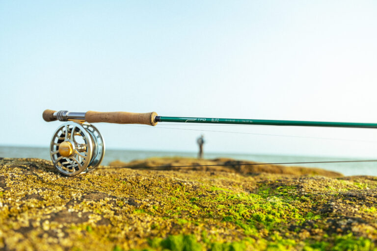 Fishing rod and reel on a rocky shore with a blurred figure in the background