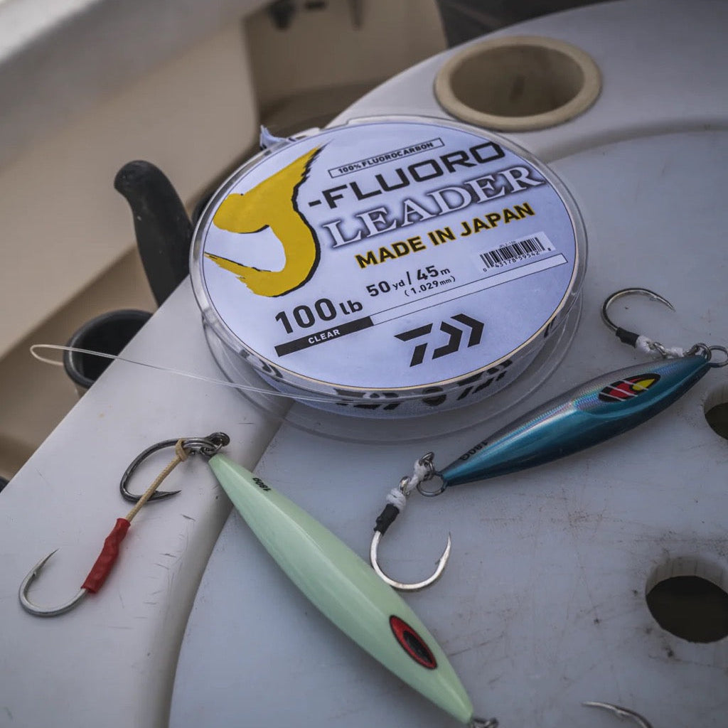 Spool of Daiwa Fluoro Leader fishing line with fishing lures on a boat seat.